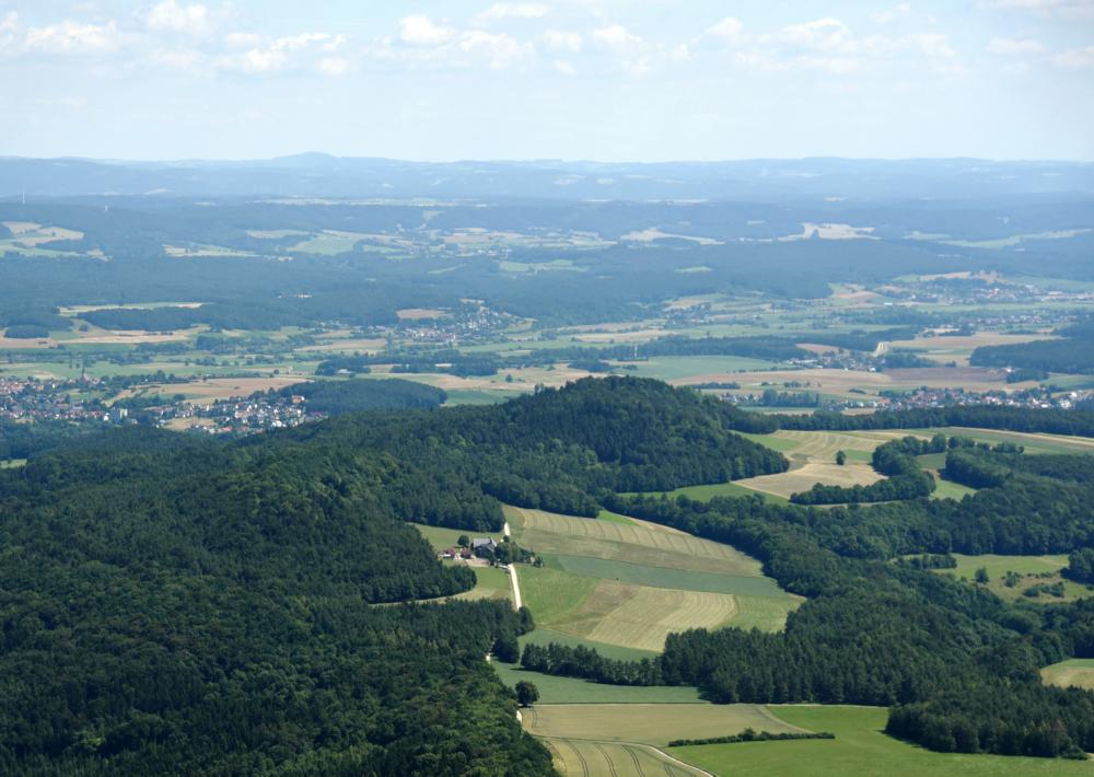 Abb. 4: Blick nach Südosten über den langgezogenen, bewaldeten Rücken des Kordigast. Der Weiler in der Mitte des Bildes ist die Steinerne Hochzeit. Im Hintergrund ist Altenkunstadt zu sehen.