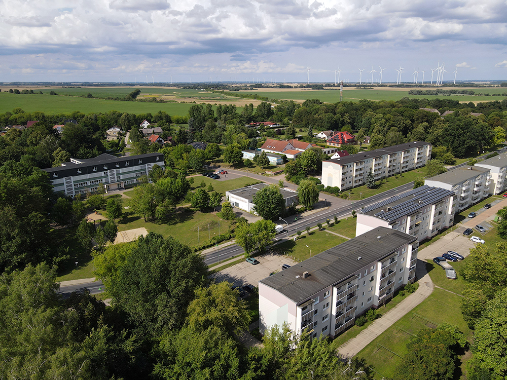 Abb. 1: Schrägluftaufnahme der Ortsmitte von Dedelow. Blickrichtung NO. Links die ehemalige Schule, davor die Brachflächen nach Abriss von Funktionsgebäuden, das leer stehende ehemalige Kaufhaus und rechts die typischen Geschosswohnungsbauten an der Woldegker Straße.