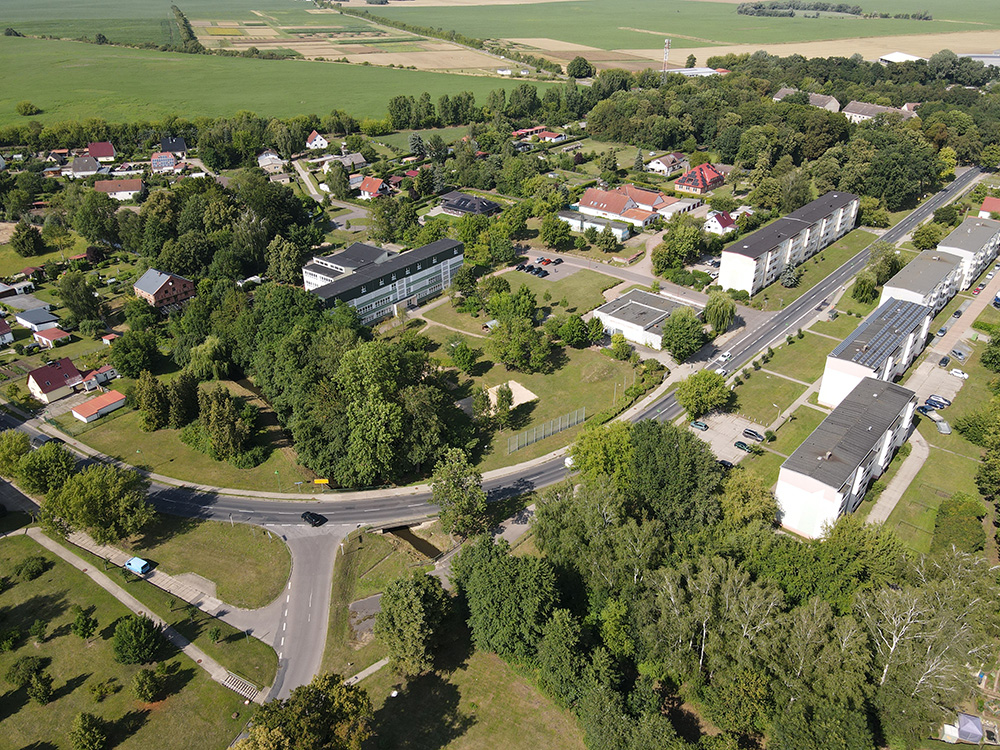 Abb. 1: Schrägluftaufnahme der Ortsmitte von Dedelow. Blickrichtung NO. Links die ehemalige Schule, davor die Brachflächen nach Abriss von Funktionsgebäuden, das leer stehende ehemalige Kaufhaus und rechts die typischen Geschosswohnungsbauten an der Woldegker Straße.